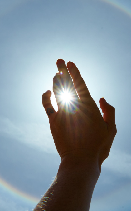 Hand silhouette against sunlit rainbow sky