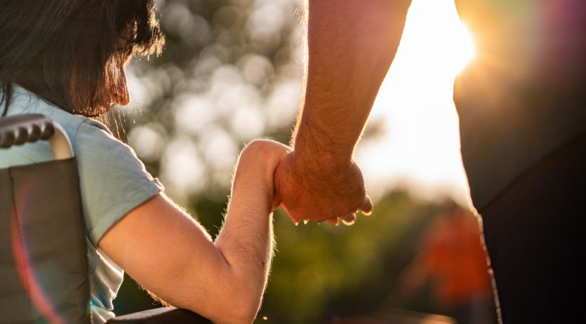 Woman in wheelchair holding caregiver's hand