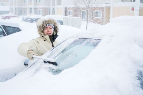 Person clearing snowy car windshield