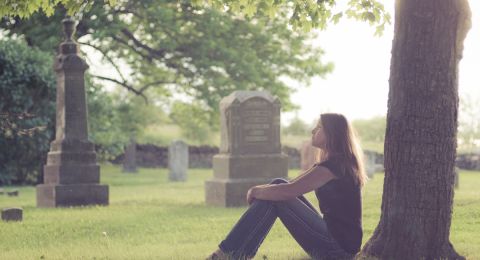 Woman sits alone at cemetery tree