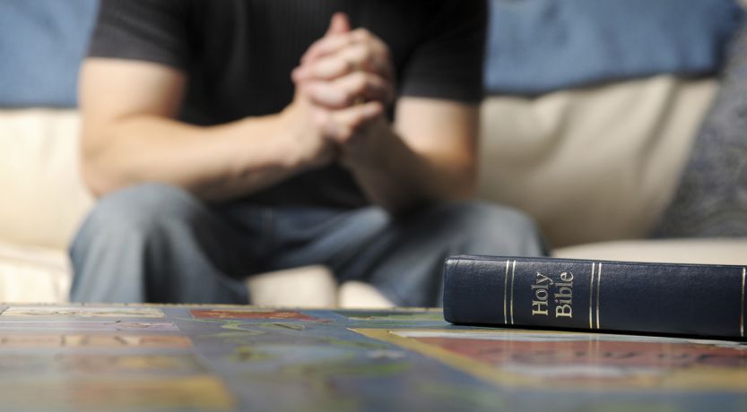 Man praying beside open Bible