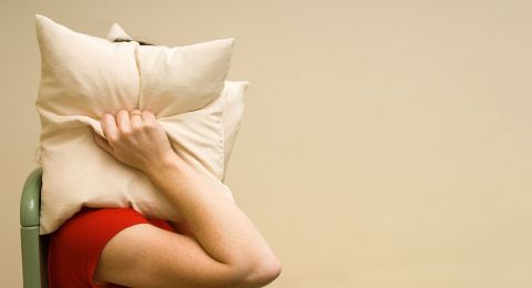 Woman hiding face behind pillow